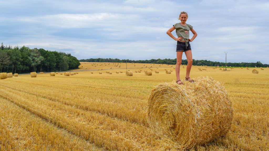 Ein selbstbewusstes Mädchen steht auf einem Strohballen auf einem Feld