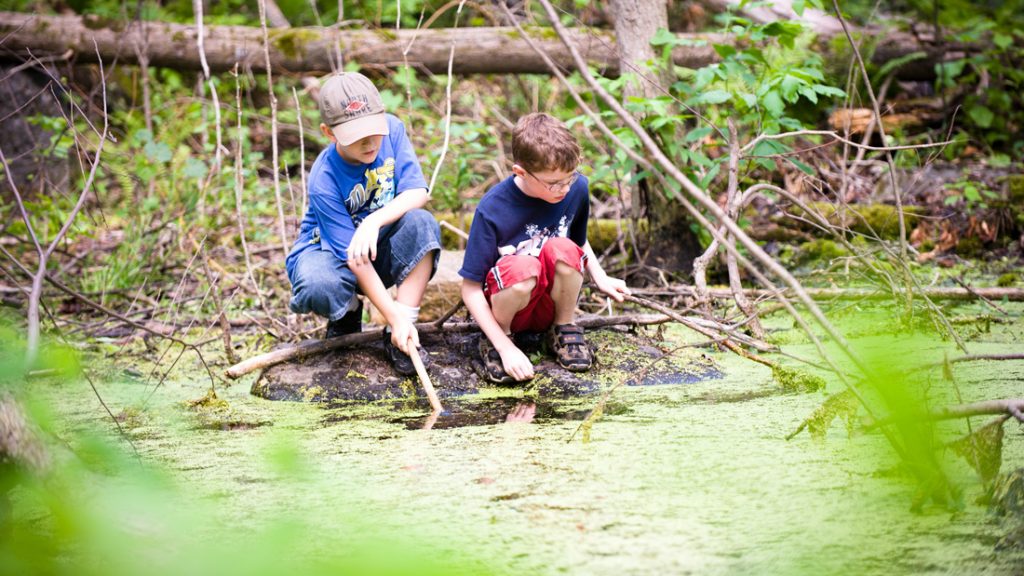 Zwei naturverbundende Jungs spielen mit Stöckern am Wasser eines Sees